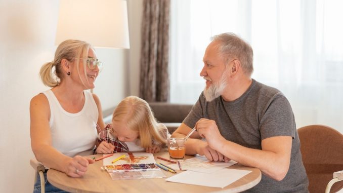 Grandparents and a child bond over painting at a cozy home setting, smiling and focused.